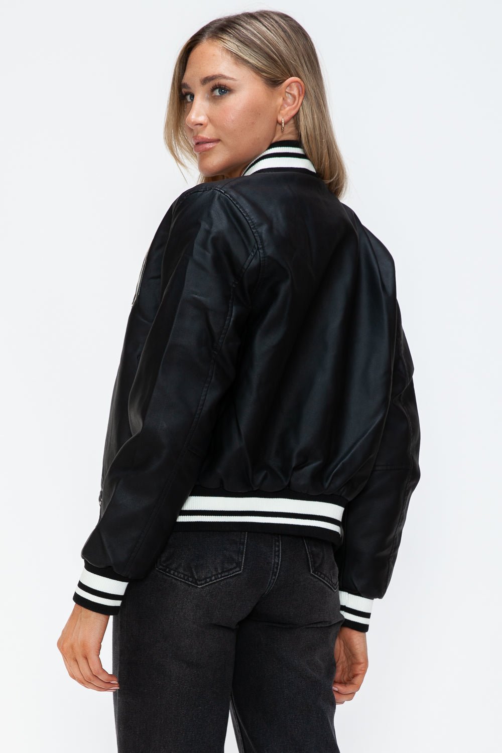 Woman wearing a Midnight Black PU Leather Contrast Snap Down Bomber Jacket, showcasing back view and striped ribbed cuffs.