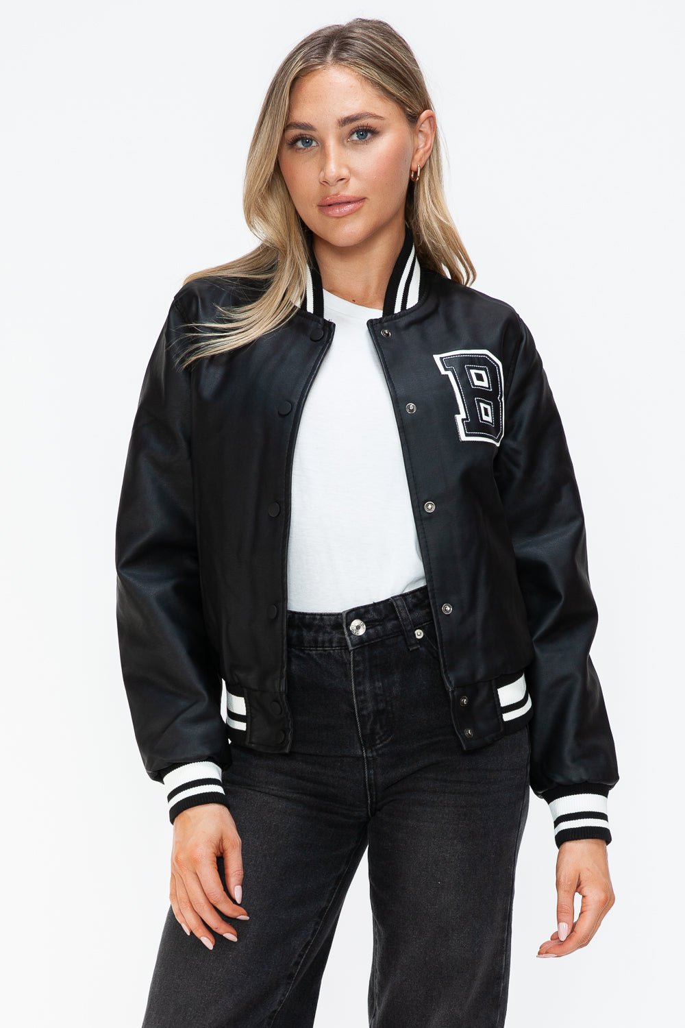 Woman wearing midnight black PU leather bomber jacket with contrast snap buttons and letter patch.