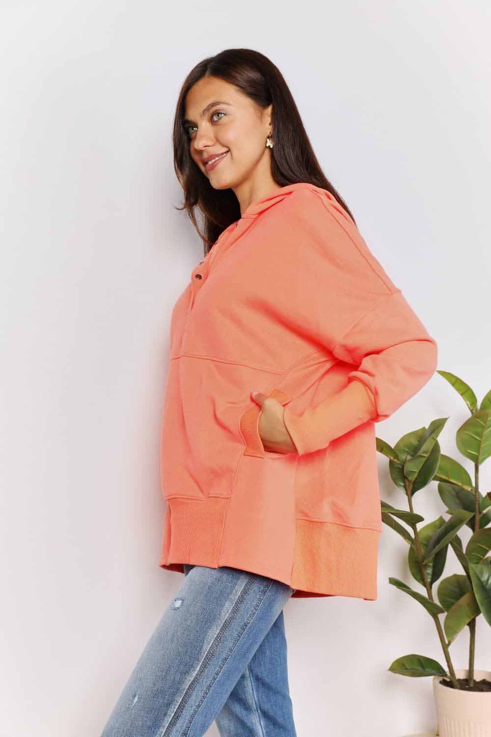 Woman in coral quarter-snap hoodie with pockets and buttoned neckline, paired with jeans, showcasing casual and comfy fashion.