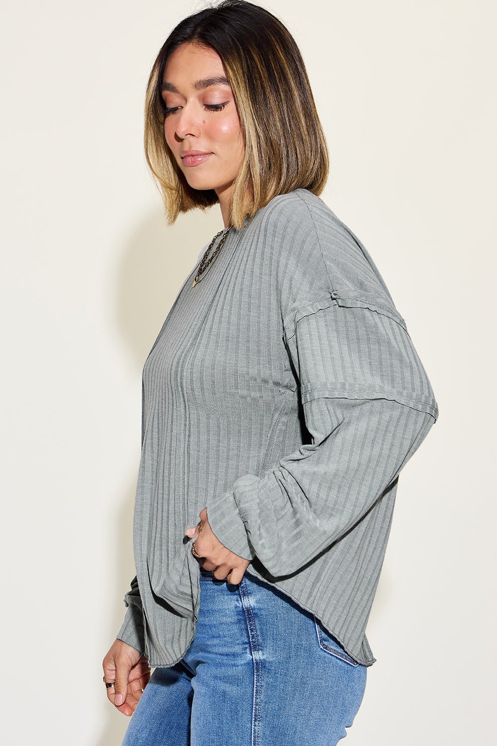 Woman wearing a ribbed round neck long sleeve t-shirt in gray with exposed seams, styled casually with blue jeans.