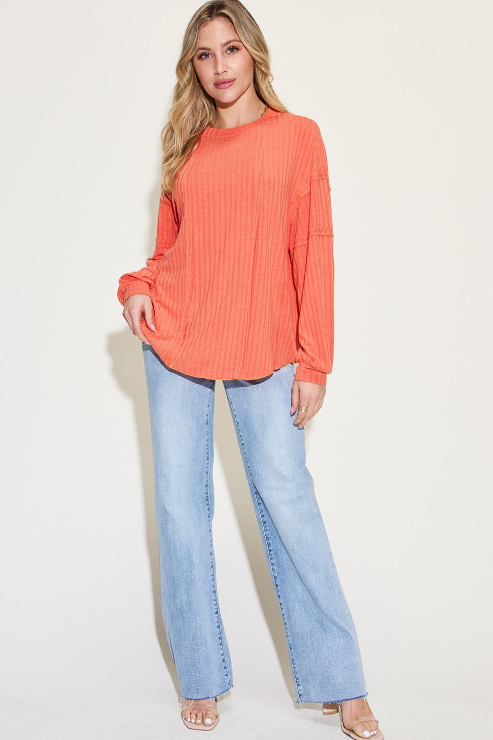Woman wearing ribbed round neck long sleeve orange t-shirt with exposed seam and jeans. Opaque fabric, moderate stretch.