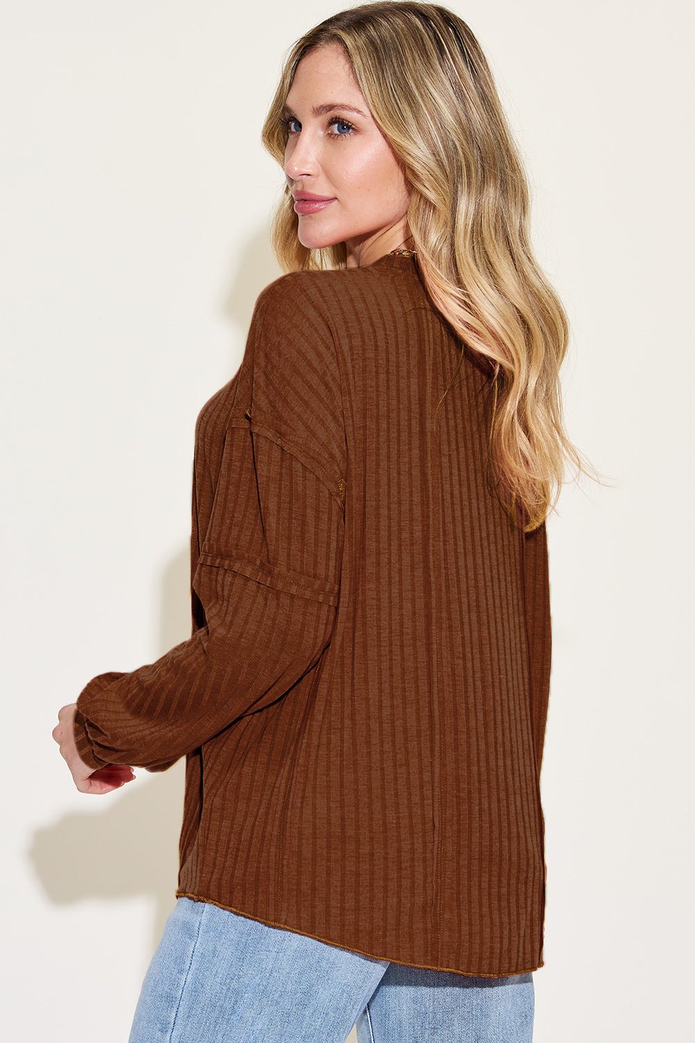 Woman wearing a brown ribbed round neck long sleeve t-shirt with exposed seams paired with light denim jeans.