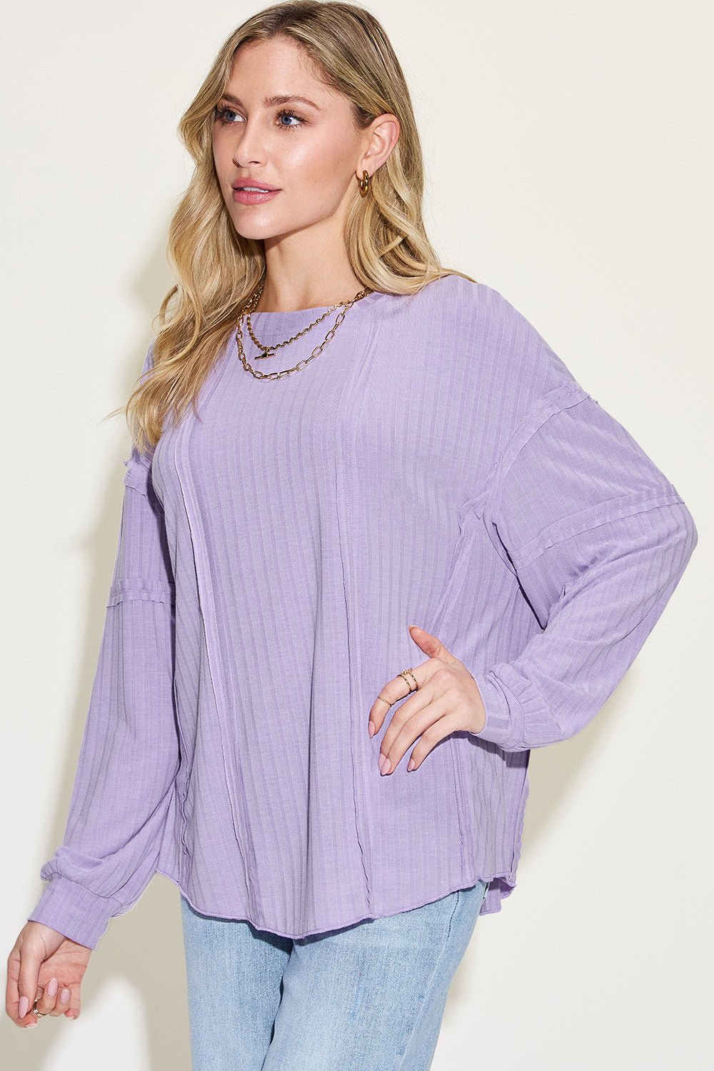 Woman wearing a ribbed round neck long sleeve lavender t-shirt with exposed seam detail, paired with light denim jeans.