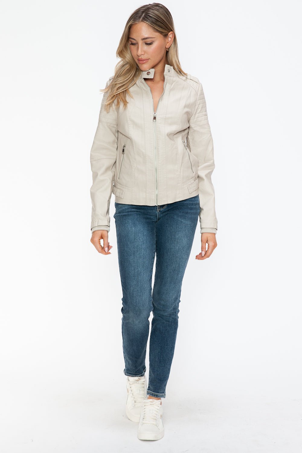 Woman wearing sand PU leather biker jacket with side zip pockets, paired with jeans and sneakers, showcasing a basic style.