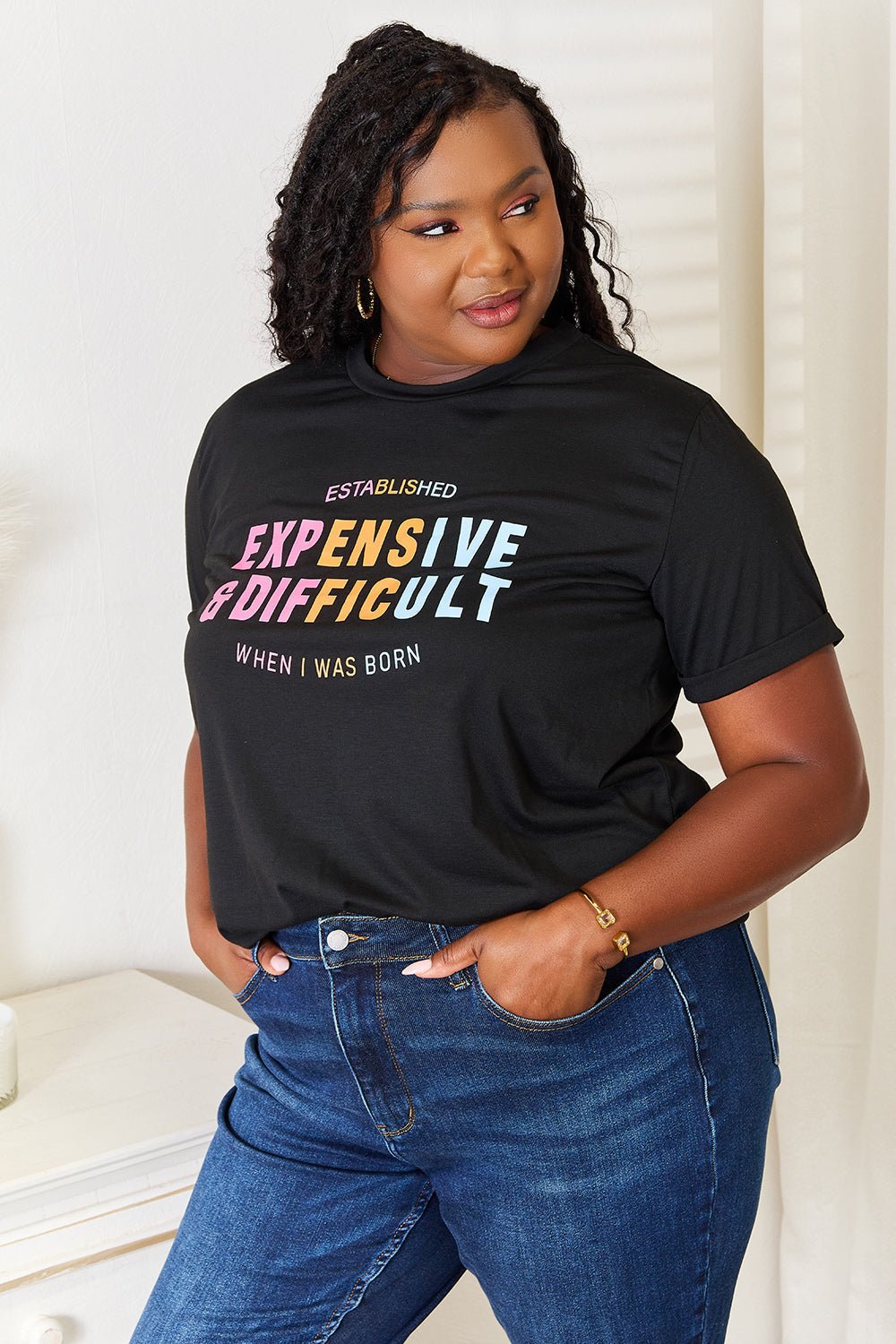 Woman wearing a slogan graphic cuffed sleeve T-shirt with jeans, standing indoors.