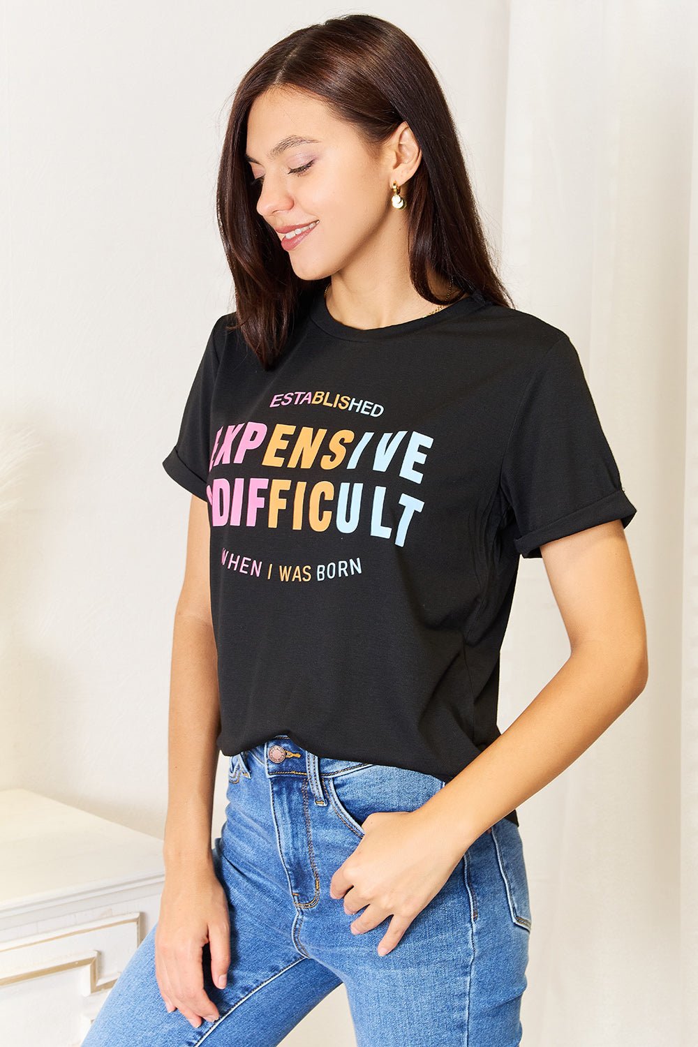 Woman wearing a black slogan graphic cuffed sleeve t-shirt with colorful lettering, paired with blue jeans.