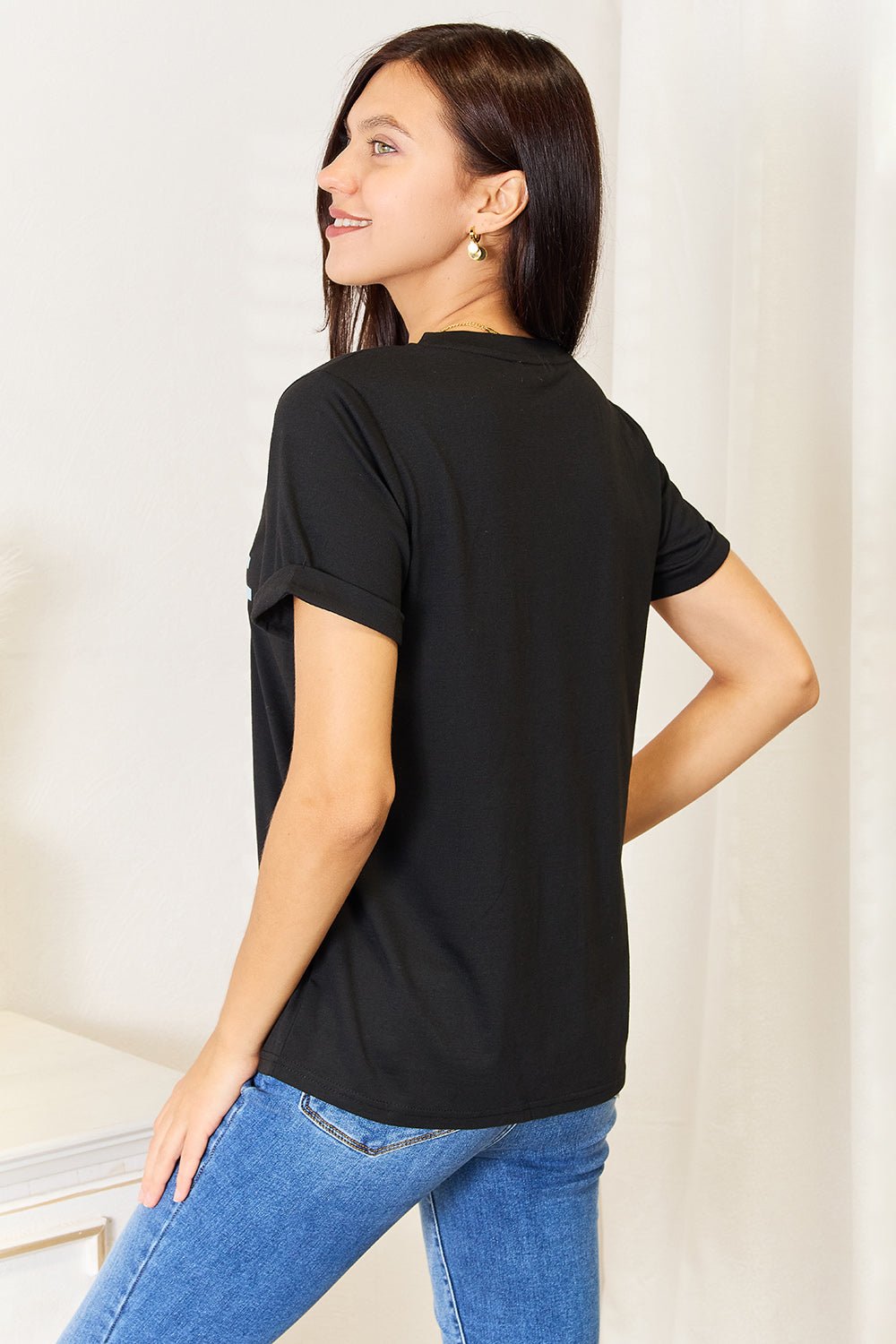 Woman wearing a black slogan graphic cuffed sleeve T-shirt with jeans, showcasing the versatile and flattering design.