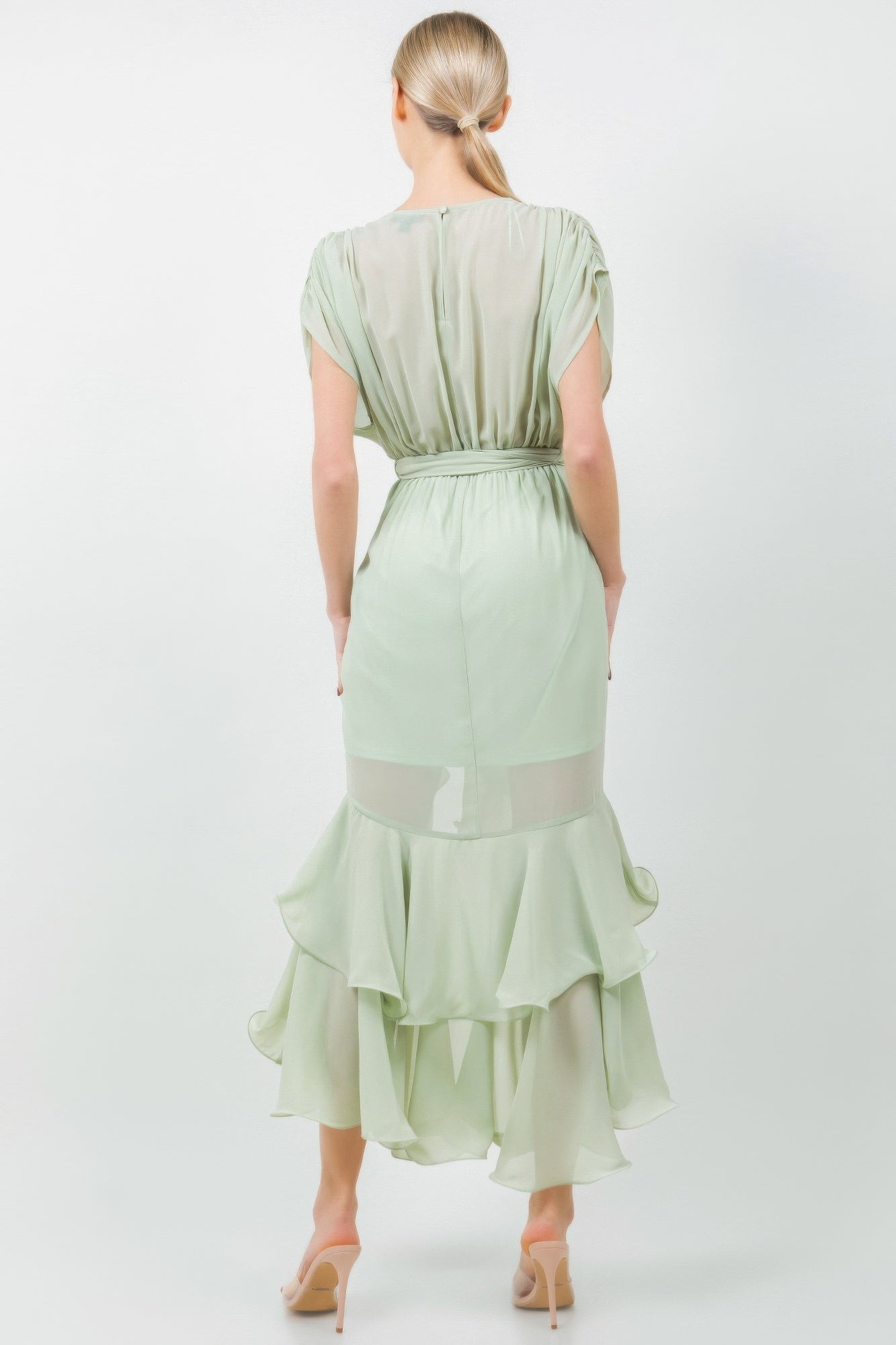 Back view of a woman wearing a light green midi dress with a tie waist and ruffle hem, highlighting elegant and feminine style.