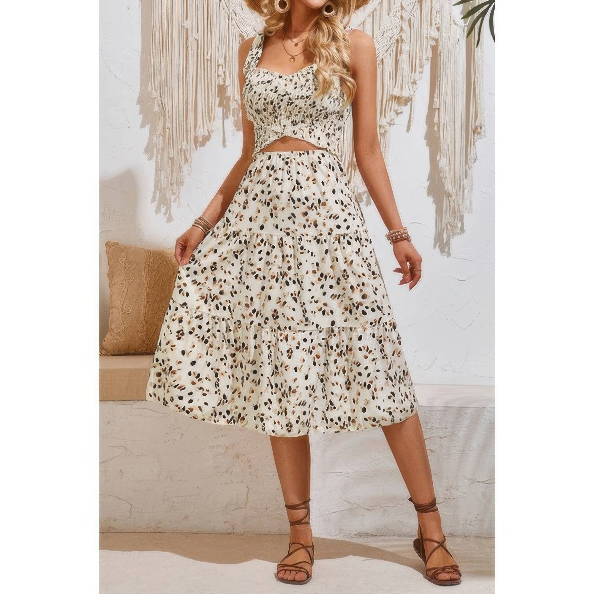 Woman in cream-colored leopard print midi dress with cutout waist detail and tie straps, wearing brown strappy sandals, standing in boho-style...