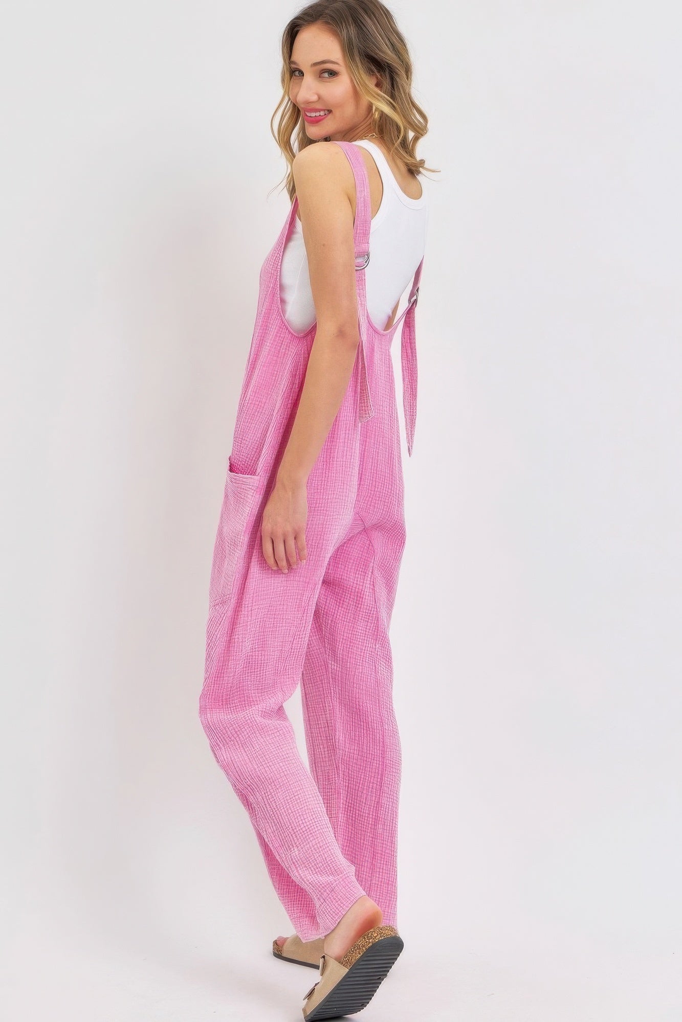 Woman wearing pink mineral-washed summer jumpsuit with adjustable straps and oversized pockets, showcasing relaxed and stylish fit.