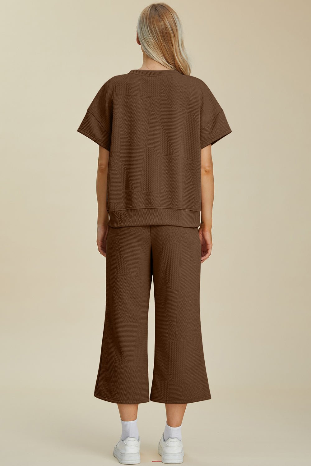 Woman wearing textured brown round neck top and pants set, slightly stretchy two-piece with drawstring, viewed from the back.