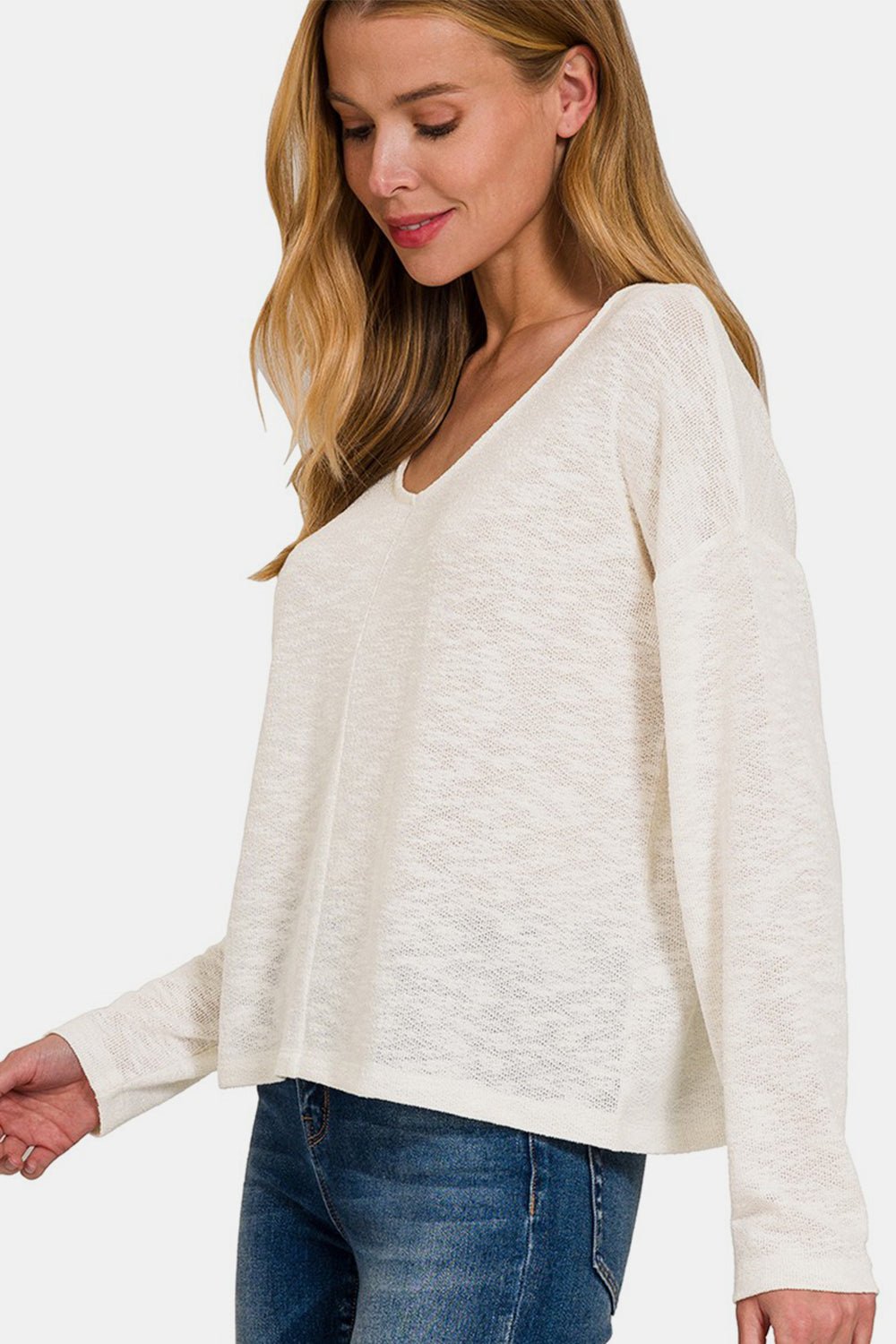 Woman wearing a white V-neck dropped shoulder long sleeve T-shirt with blue jeans.