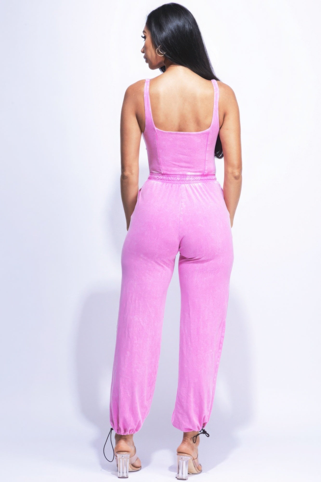 Woman wearing pink jumpsuit with adjustable ankles, back view showcasing relaxed fit and chic silhouette.