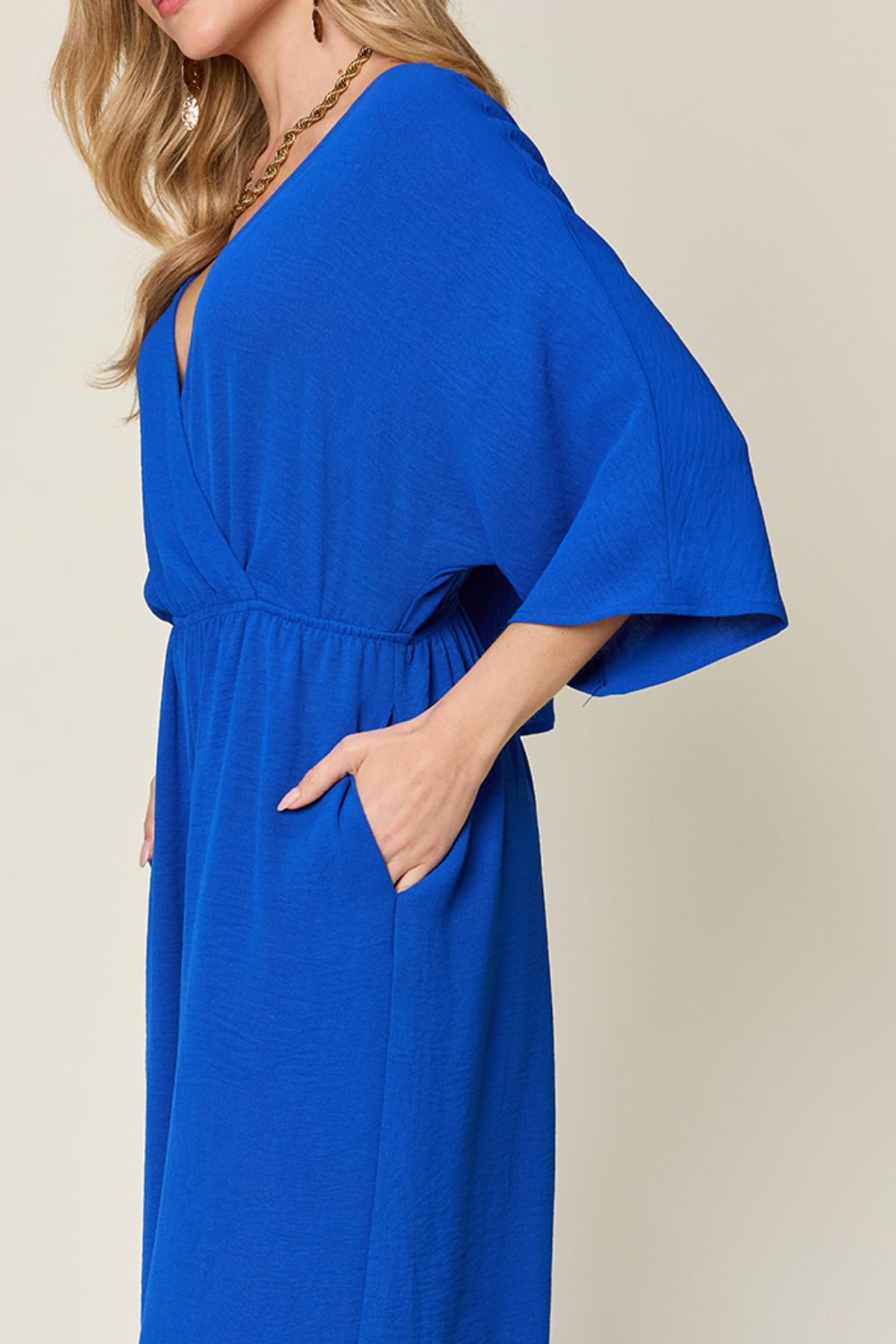 Elegant blue surplice wide leg jumpsuit with pockets, featuring tied and ruched details, made of 95% polyester and 5% spandex