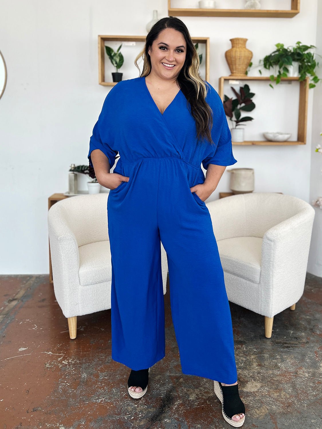 Woman wearing blue surplice wide leg jumpsuit with pockets, featuring tie and ruched details for stylish comfort.
