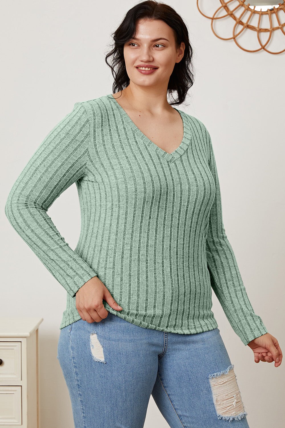 Woman wearing green ribbed V-neck long sleeve T-shirt with ripped jeans, smiling confidently.